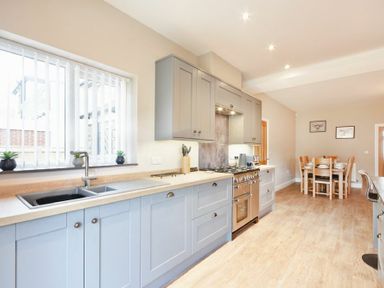 A kitchen with blue cabinets a sink stove and a dining table with chairs at Bradacar in Seahouses