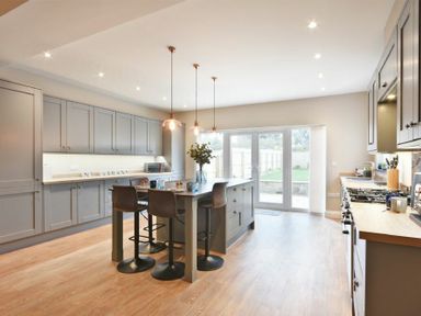A kitchen with gray cabinets a central island with chairs and pendant lights at Bradacar in Seahouses