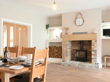 A dining area with a wooden table set with dishes and glasses next to a brick fireplace with stacked firewood at Bradacar in Seahouses