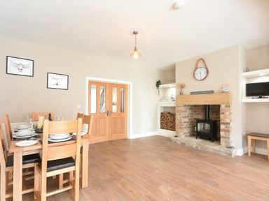 A dining room with a wooden table and chairs near a brick fireplace with a stove and a clock above at Bradacar in Seahouses