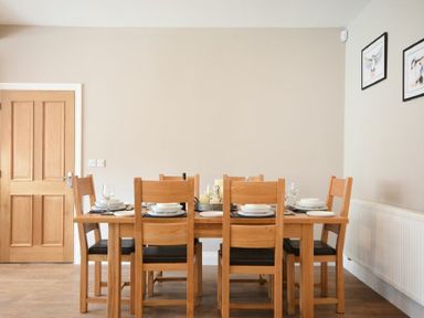 A dining room with a wooden table set for six and wooden chairs with black seats at Bradacar in Seahouses