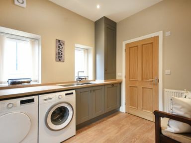 A laundry room with washing machine and dryer under a counter with sink and cabinets at Bradacar in Seahouses