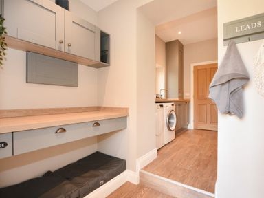 A laundry room with washing machine and dryer under a wooden countertop and cabinets above at Bradacar in Seahouses
