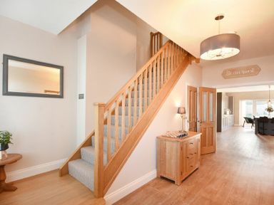 A hallway with wooden stairs carpeted steps a wooden sideboard with a lamp and chessboard a small round table with a plant and mirror on the wall at Bradacar in Seahouses