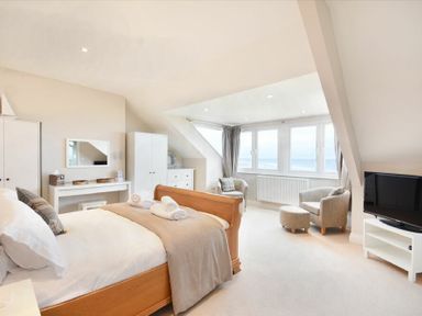 A bedroom with a wooden bed a dressing table a wardrobe two armchairs a television and large windows overlooking the sea at Bradacar in Seahouses