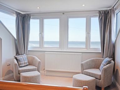 A seating area with two armchairs and footstools facing windows overlooking the sea with curtains at Bradacar in Seahouses