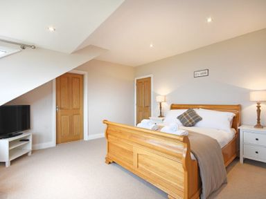 A bedroom with a wooden bed, two bedside tables with lamps, a television on a stand, and two wooden doors at Bradacar in Seahouses