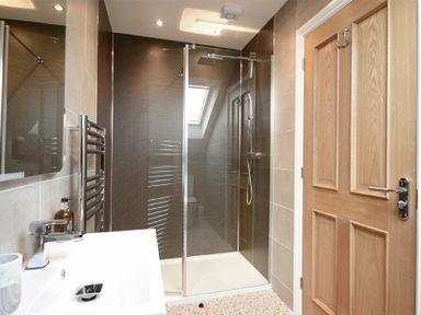 A bathroom with a shower and a wooden door at Bradacar in Seahouses