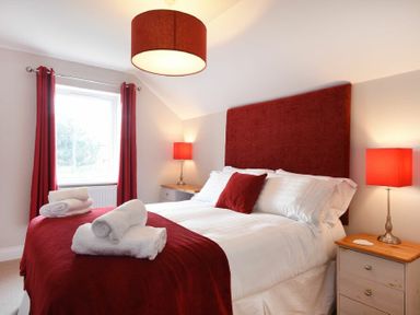 A bedroom with a double bed red headboard red throw red curtains and red lamps at Bradacar in Seahouses