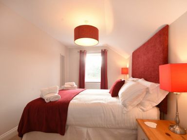 A bedroom with a bed with red headboard and red bed cover with folded towels on top at Bradacar in Seahouses