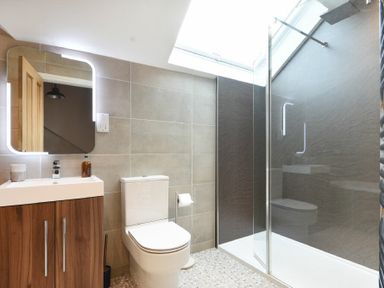 A bathroom with a wall-mounted mirror above a wooden vanity unit a toilet and a glass-enclosed shower at Bradacar in Seahouses