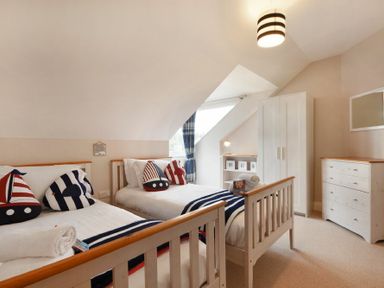 A bedroom with two single beds pillows and striped blankets a wardrobe a chest of drawers and a window at Bradacar in Seahouses