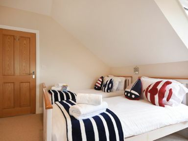 A bedroom with two single beds with striped bedding and nautical themed cushions at Bradacar in Seahouses