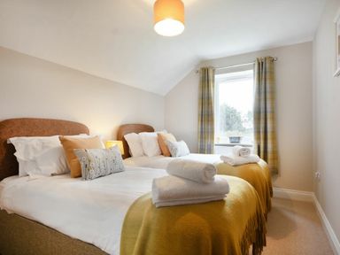 A bedroom with two single beds with pillows and folded towels near a window with curtains at Bradacar in Seahouses