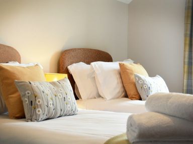A bedroom with two beds with headboards pillows and folded towels at Bradacar in Seahouses