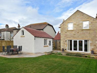 A backyard with patio furniture a lawn and two houses at Bradacar in Seahouses