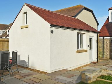 A small white building with a red tiled roof and patio furniture on a stone patio at Bradacar in Seahouses
