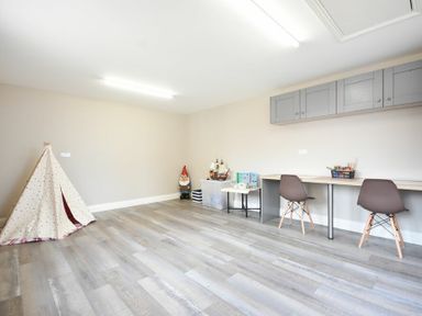 A playroom with a small fabric teepee toy storage boxes a table with craft supplies two chairs and wall cabinets at Bradacar in Seahouses