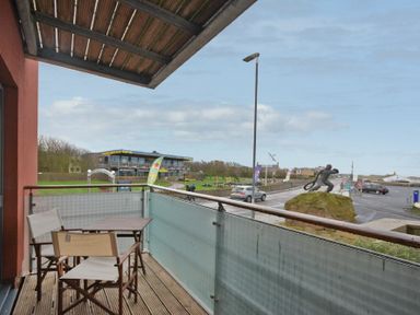 A balcony with two chairs and a table overlooking a street with a statue on a rock and a building in the background at Castle View at the Viking in Seahouses
