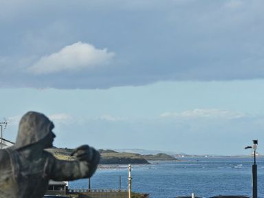 A coastal view with a statue in the foreground and ocean with hills in the background at Castle View at the Viking in Seahouses