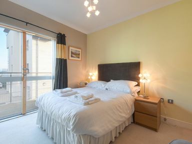 A bedroom with a double bed bedside tables lamps and a sliding glass door at Castle View at the Viking in Seahouses