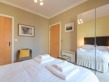 A bedroom with a double bed and towels on it two wooden doors a gray chair with a yellow cushion and mirrored wardrobe doors at Castle View at the Viking in Seahouses