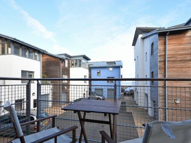 A balcony with two chairs and a table overlooking modern residential buildings at Castle View at the Viking in Seahouses