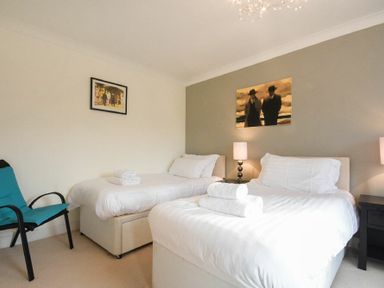 A bedroom with two single beds towels on beds a blue chair and two paintings on walls at Castle View at the Viking in Seahouses