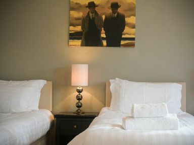 A bedroom with two single beds white bedding a bedside table lamp and a painting above at Castle View at the Viking in Seahouses