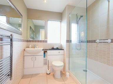A bathroom with a shower enclosure toilet sink and storage cabinets at Castle View at the Viking in Seahouses
