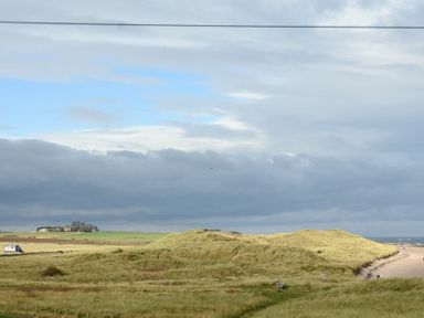 A sandy beach with grassy dunes and a castle in the distance at Castle View at the Viking in Seahouses