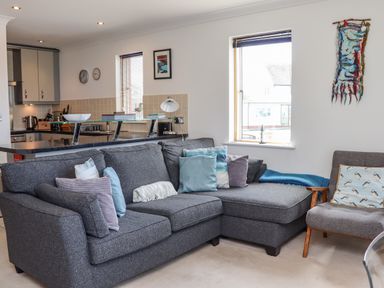 A living room with a gray sectional sofa and cushions next to a kitchen with a counter and cabinets at Castle View at the Viking in Seahouses
