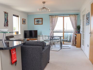 A living room with a sofa a TV a glass dining table with chairs and a balcony at Castle View at the Viking in Seahouses