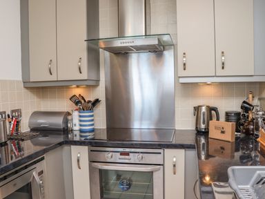 A kitchen with an electric stove oven range cooker steel backsplash and hood white cabinets kettle and utensils on the counter at Castle View at the Viking in Seahouses
