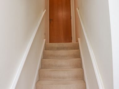 A carpeted staircase with white walls and handrails leading to a closed wooden door at Castle View at the Viking in Seahouses
