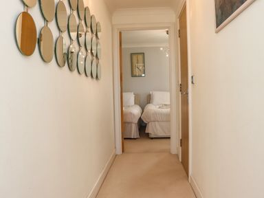 A hallway with circular mirrors on the left wall leading to a bedroom with two single beds at Castle View at the Viking in Seahouses