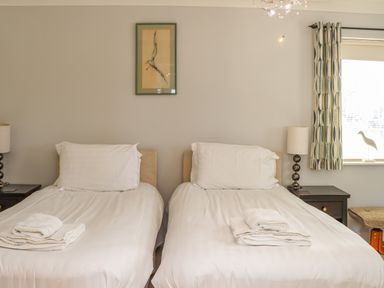 A bedroom with two single beds with white bedding and towels on each bed two bedside tables with lamps and a window with patterned curtains at Castle View at the Viking in Seahouses