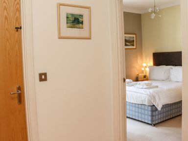 A bedroom with a bed with white bedding and towels on top seen through a partially open door at Castle View at the Viking in Seahouses