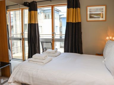A bedroom with a bed with folded towels on it next to a window with curtains and a chair on the balcony at Castle View at the Viking in Seahouses