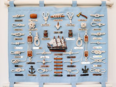 A display of various nautical knots with labels on a blue fabric background with a model ship and small anchors