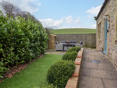 An outdoor patio area with seating and table beside a stone building and hedge at The Old Stables in Bamburgh