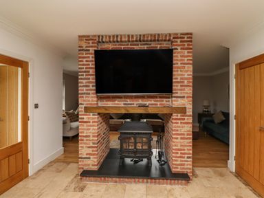 A brick fireplace with a wood stove and a mounted TV above it between two wooden doors at The Old Stables in Bamburgh