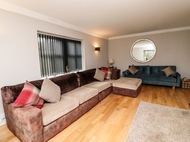 A living room with two sofas a large round mirror and window blinds at The Old Stables in Bamburgh
