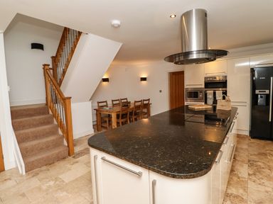 A kitchen with an island and black countertop near a wooden staircase and dining table at The Old Stables in Bamburgh