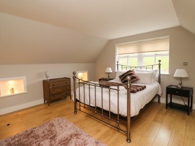 A bedroom with a metal bed frame wooden chest of drawers two bedside tables with lamps and a pink rug at The Old Stables in Bamburgh