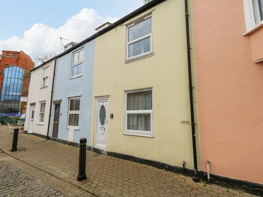 A row of terraced houses with different colored facades on a paved street at Cove Street Cottage in Weymouth