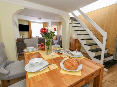 A dining table set with plates bowls glasses and bread next to stairs and a living room at Cove Street Cottage in Weymouth