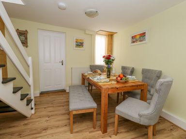 A dining room with a wooden table set for a meal with gray chairs and a bench near stairs at Cove Street Cottage in Weymouth