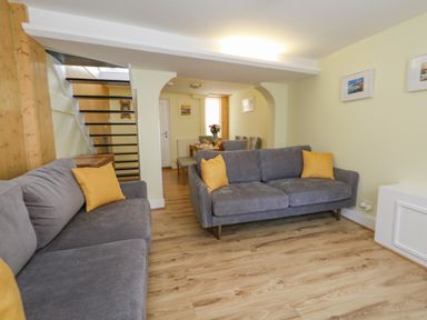 A living room with two gray sofas with yellow cushions and a dining area with a wooden table and chairs at Cove Street Cottage in Weymouth