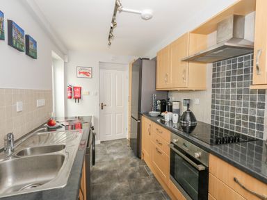 A kitchen with wooden cabinets a black countertop a stainless steel oven a sink and kitchen appliances at Cove Street Cottage Weymouth
